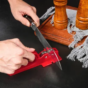 Close-up detail of manual kitchen knife sharpener in action, showing red plastic body and wheels.