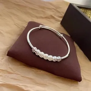 Bracelet jonc en métal argenté avec design de breloques pièces vintage, bijoux minimalistes.