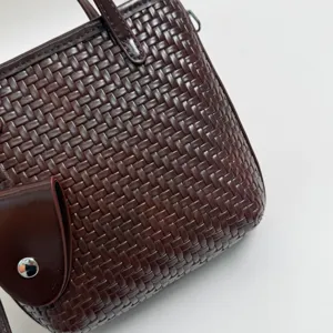 Καφέ πλεκτή τσάντα λεπτομέρεια κοντινό πλάνο δείχνει λεπτή υφή δέρματος και μεταλλικό κούμπωμα.
