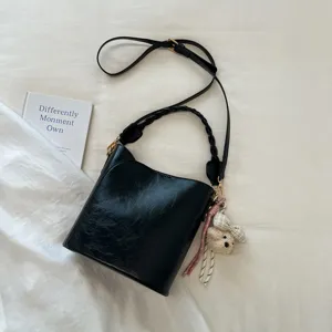 Détail de sac seau en cuir noir avec poignée tressée et charm charmant ours sur fond blanc.