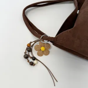 Braune Wildleder-Umhängetasche mit geflochtenem Blumenanhänger und Holzperlen.