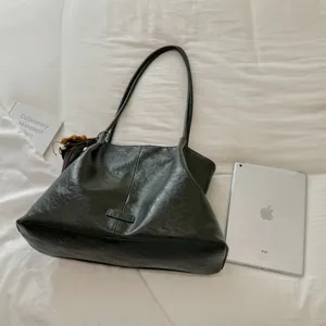 Detail shot of dark green retro leather tote bag on white fabric with tablet prop.