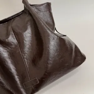 Close-up detail of dark brown glossy crinkled leather tote bag, showing soft slouchy design.