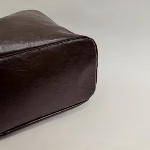 Close-up detail of dark brown leather tote bag corner showing fine texture and stitching.