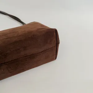 Detail shot of brown suede shoulder bag bottom corner, showing fine stitching and texture.