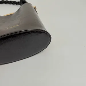 Vue détaillée du sac seau en cuir noir avec poignée tressée et détails en métal doré.