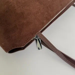 Brown suede handbag detail, metal zipper and strap close-up view for daily commuting.