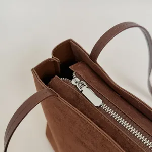 Close-up detail of brown suede tote bag featuring silver metal zipper and slim shoulder straps.
