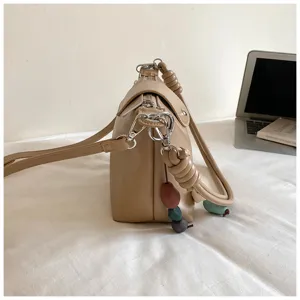 Beige retro shoulder bag side view, showcasing knotted handle and colorful bead charm details.