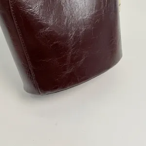 Détail de sac seau rétro marron foncé, sac à main tendance en cuir verni froissé.