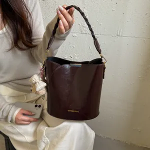 Vue rapprochée du sac seau marron foncé avec poignée tressée et charmant pendentif d'ours.