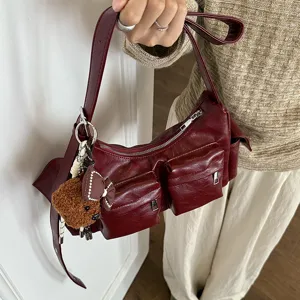 Close-up detail of the burgundy multi-pocket shoulder bag with cute bear charm and zipper.