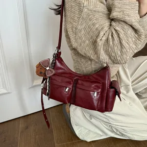 Burgundy leather multi-pocket shoulder bag detail, stylish commuter crossbody design with charm.