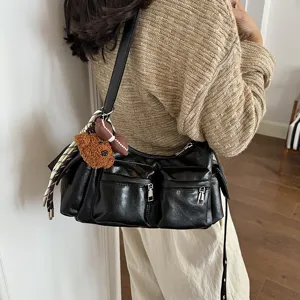 Detail view of stylish black multi-pocket shoulder bag with cute bear pendant and strap.