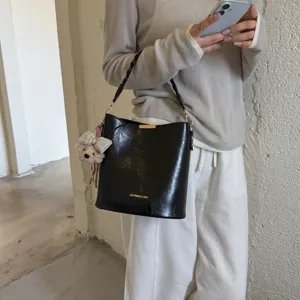 Détail de sac seau en cuir PU noir, avec poignée tressée et charmant pendentif d'ours mignon.