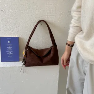 braune Wildleder-Achseltasche Detailansicht mit Anhänger in minimalistischer Kulisse