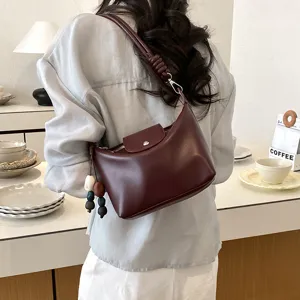 Detailed view of maroon shoulder bag with beaded strap and pendant, worn in a clean interior.