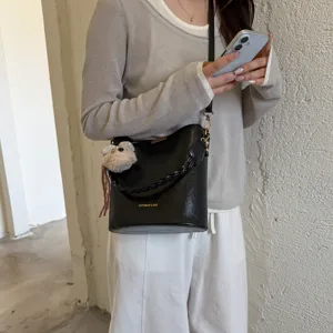 Sac seau en cuir PU noir avec poignée tressée et charm d'ours mignon pour la mode féminine.