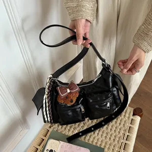 Black leather multi-pocket shoulder bag detail showing cute bear charm and woven strap.