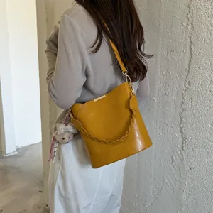 Sac seau rétro en cuir jaune avec poignée tressée et pendentif ours pour les femmes.