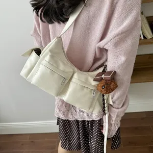 Detailed view of the chic cream multi-pocket shoulder bag with cute plush charm.