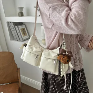 Detail view of a stylish white multi-pocket shoulder bag with cute bow plush bear keychain.