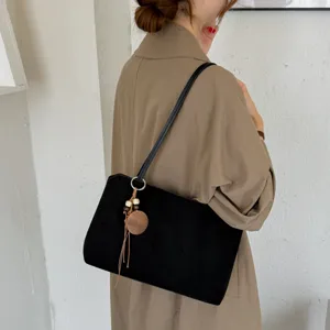 Detail view of a woman carrying a black suede shoulder bag with a stylish wooden pendant.