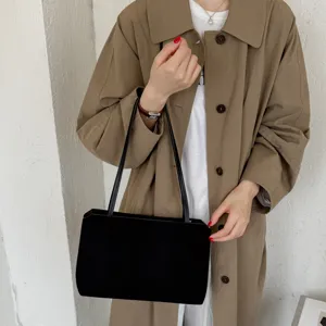 Close-up of a stylish black underarm shoulder bag worn with a chic khaki trench coat.