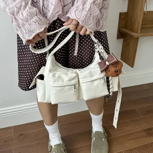 White multi-pocket shoulder bag detail showing front zipper pockets and bear pendant.
