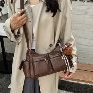 Detailed view of brown leather shoulder bag with multi pockets and cute bear pendant.