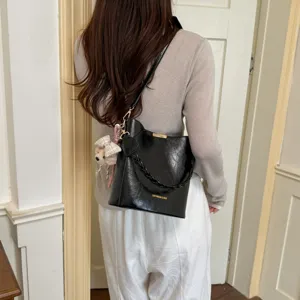 Vue détaillée du sac seau noir tendance avec poignée tressée et charmant pendentif ours au dos.