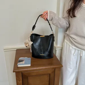 Sac seau noir élégant avec poignée tressée et pendentif ours pour la mode d'automne.