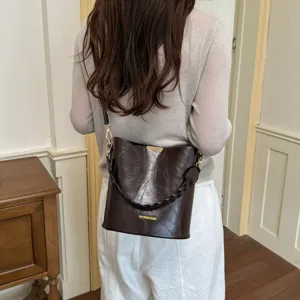 Détail de sac seau en cuir marron avec bandoulière chaîne élégante et design de mode quotidienne.