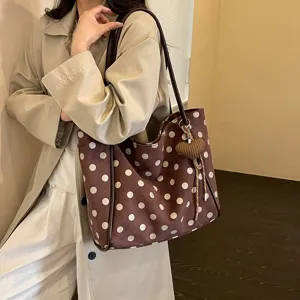 Detailed shot of brown polka dot suede tote bag featuring shoulder strap and heart charm.