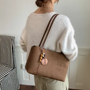 Detail shot of brown suede shoulder bag with strap and charm pendant in indoor scene.