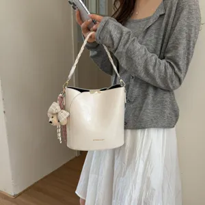 Gros plan sur les détails du sac seau blanc crème avec poignée tressée et charm d'ours.