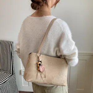 Detail shot of woman wearing a stylish beige suede shoulder bag with pendant accessory.