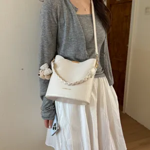 Vue détaillée du sac seau blanc élégant avec poignée tressée et charmant pendentif d'ours.
