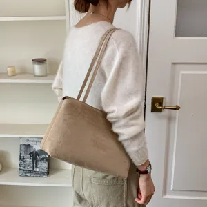 Detail shot of a minimalist brown suede shoulder bag worn by a model in an indoor setting.