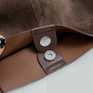 Detail shot of brown suede tote bag interior magnetic snap button closure and lining.