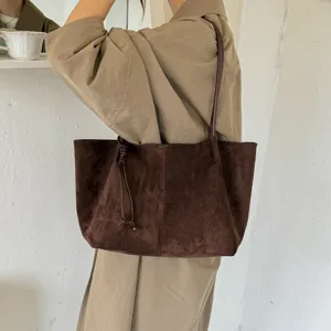 Detail view of the brown suede shoulder tote bag with thin straps and side knot decor.