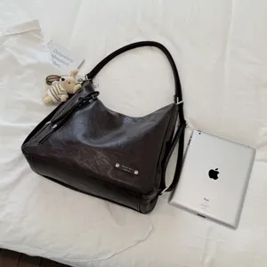 Detail view of a dark brown slouchy PU leather shoulder tote bag with a cute bear plush charm.