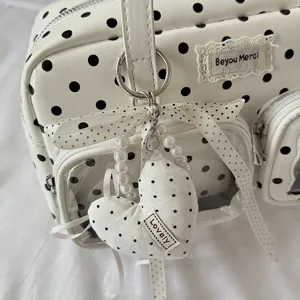 Close-up detail of white polka dot bowling bag with pearl strap and heart pendant.
