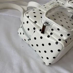 White black polka dot handbag detail closeup, featuring clear front pocket and metal zipper.