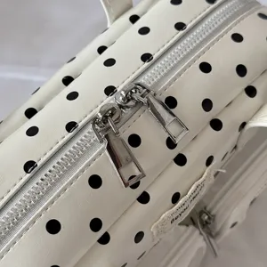 Detailed view of white polka dot bowling handbag, featuring dual metal zippers and stylish design.
