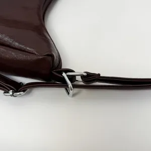 Close-up view of brown leather shoulder bag metal strap and buckle hardware details.