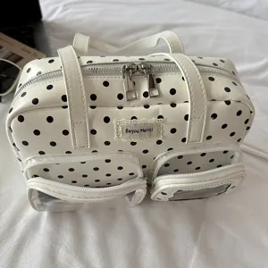 Close-up view of stylish polka dot handbag featuring dual top handles and clear pockets.