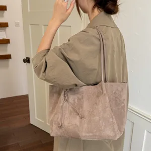 Detail shot of a taupe suede tote bag, featuring slim shoulder straps and a side knot.