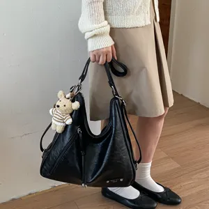 Detail shot of black leather hobo tote bag with cute bear charm and large storage capacity.