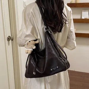 Detailed shot of dark brown soft leather slouchy shoulder bag with cute bear keychain accessory.